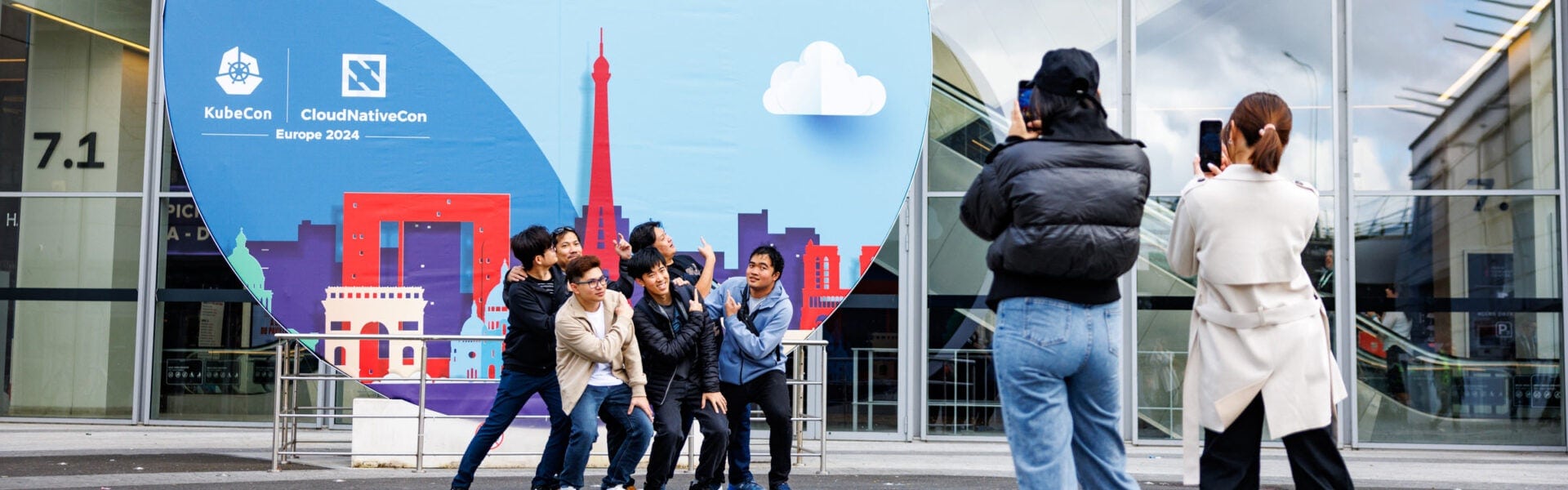 A group of 6 people posing in front of the event sign while 2 people take their photo.